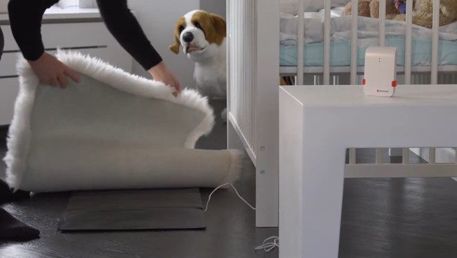 Bellman Pressure Sensor Mat Being Placed Under a Rug Next to Baby Cry Monitor